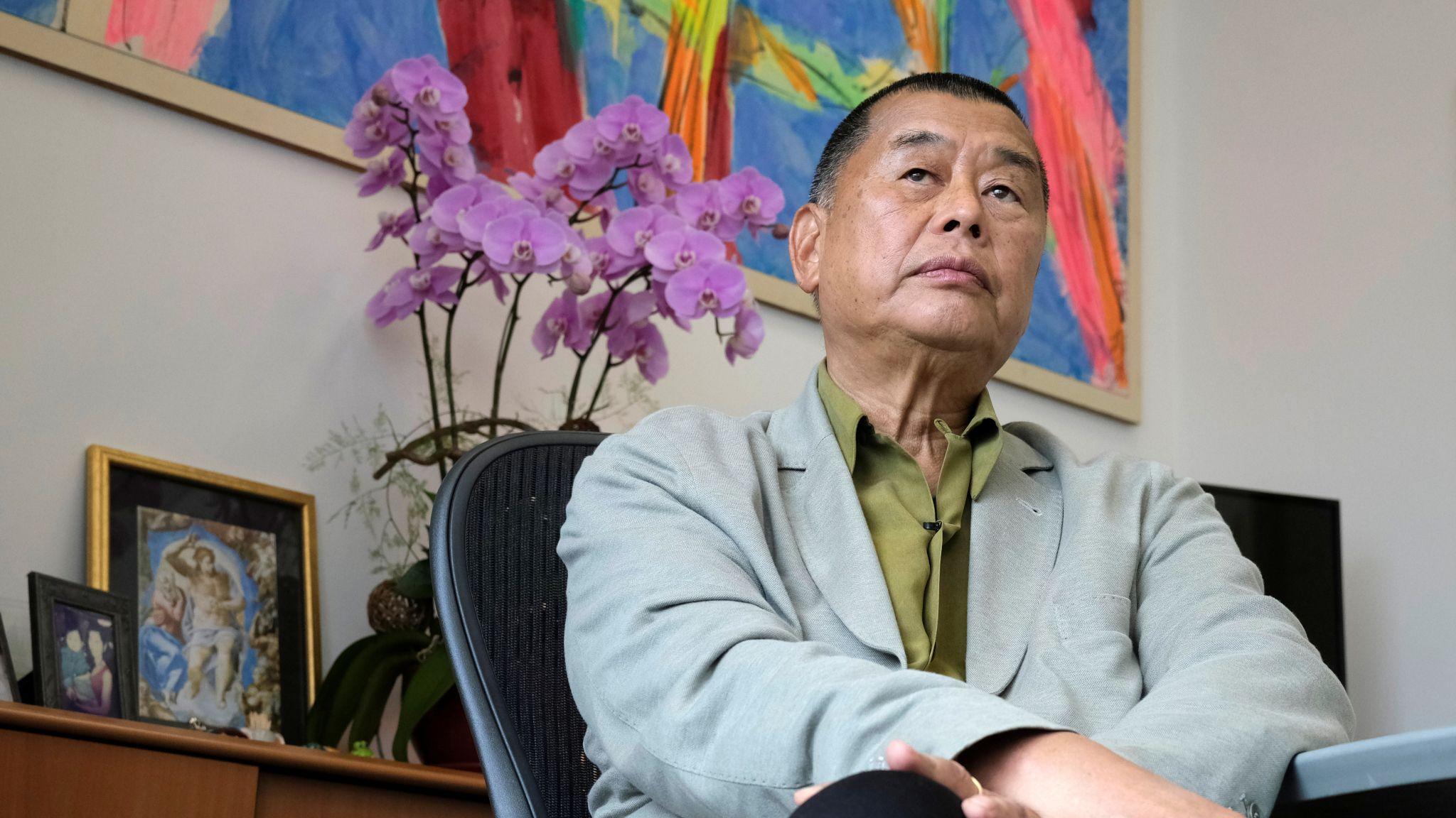黎智英身穿灰色西裝外套，綠色襯衫，坐在辦公椅上接受媒體訪問，其左邊放有一盤粉紅色蘭花（29/5/2020）