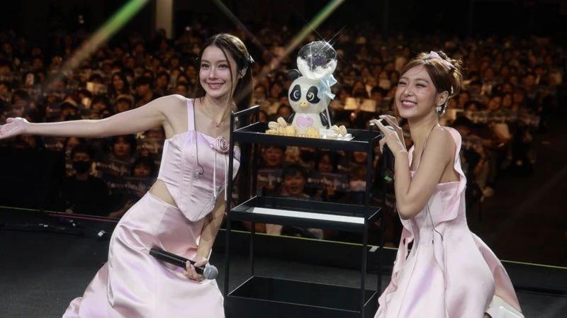 اسٹیج پر، تماشائیوں سے کھچا کھچ بھرے ہال کی طرف پیٹھ کیے، ٹپناری نم تان اور راچانن فلم کھڑی ہیں۔ ایک کے ہاتھ میں مائیکروفون ہے، اور دونوں کیمرے کی طرف دیکھ کر مسکرا رہی ہیں۔