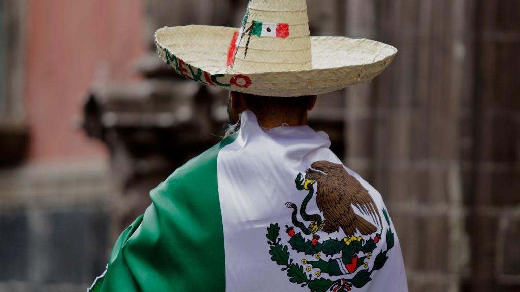 Un hombre cubre su cuerpo con una bandera de México.