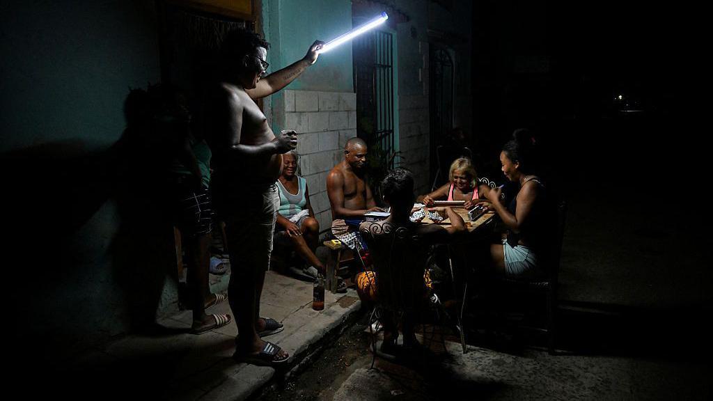 Fam&iacute;lia cubana jogando domin&oacute; &agrave; luz de uma lanterna