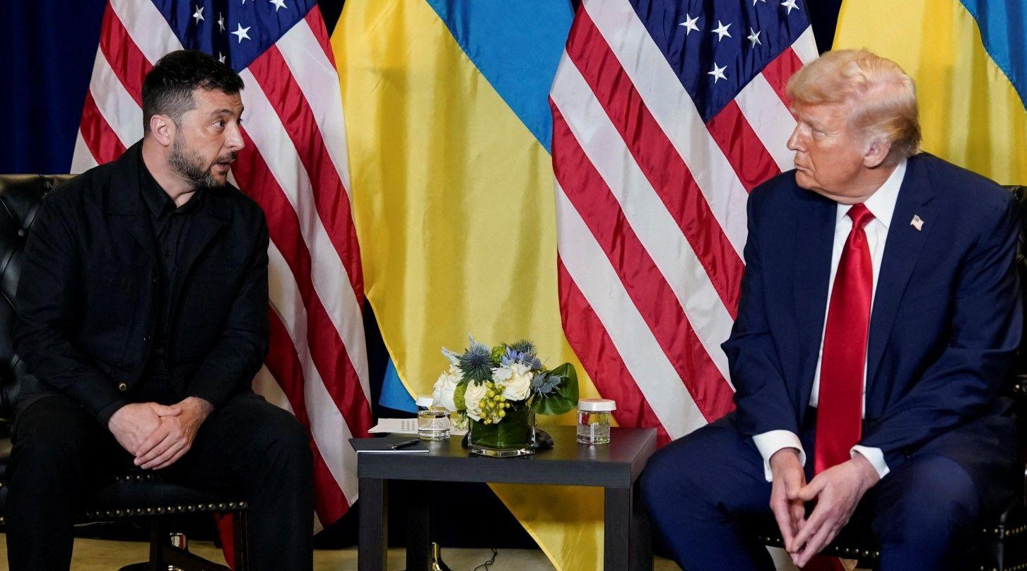 يرتدي زيلينسكي (يسار) سترة وقميصاً رسميين بلون أسود، بينما يرتدي ترامب بدلةً كحلية اللون وقميصاً أبيض وربطة عنق حمراء. يجلسان بجانب بعضهما البعض وخلف كل واحد منهما العلم الأوكراني والأمريكي.