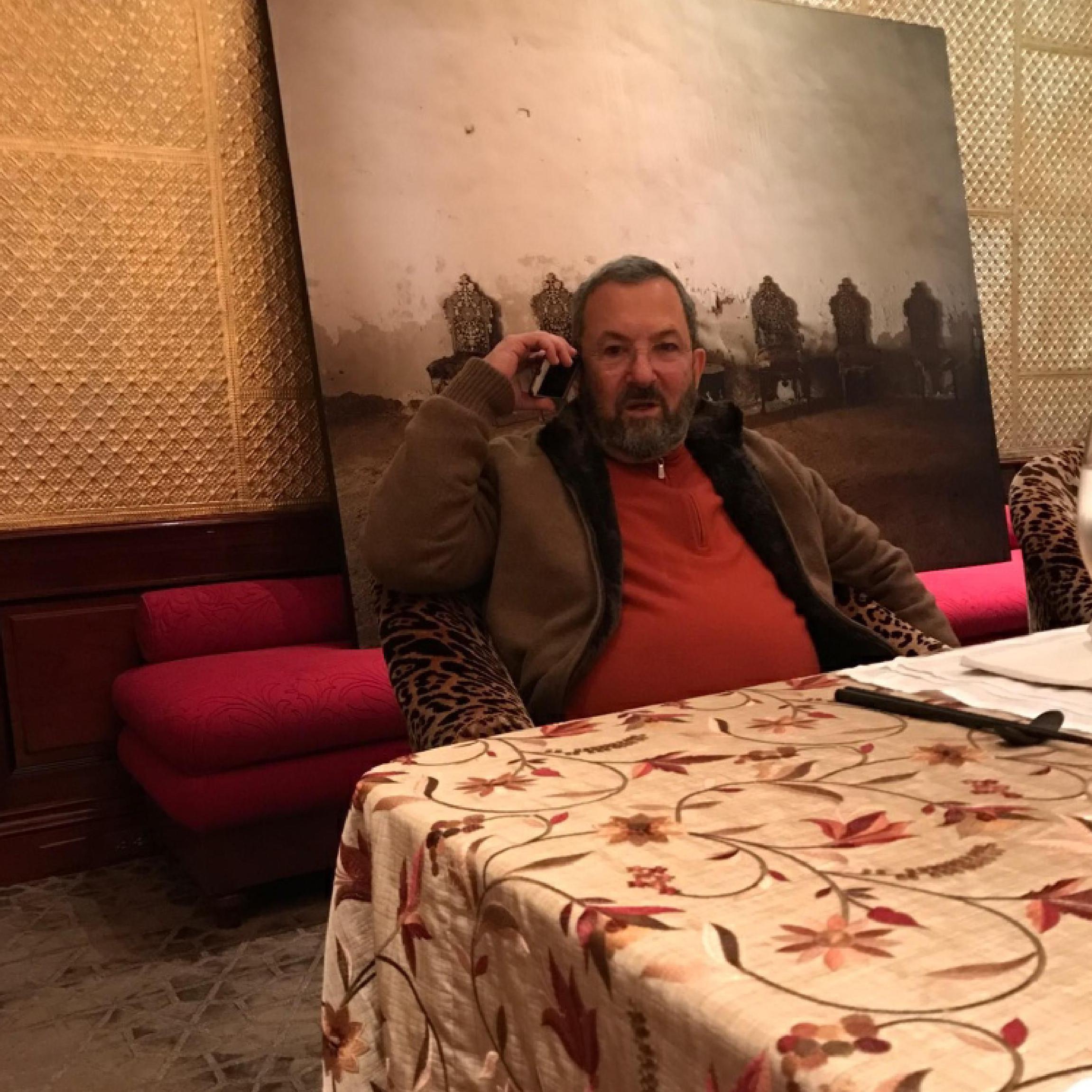 باراك يرتدي سترة برتقالية اللون ومعطفا بني اللون، ويجلس على كرسي ويتحدث عبر هاتفه المحمول