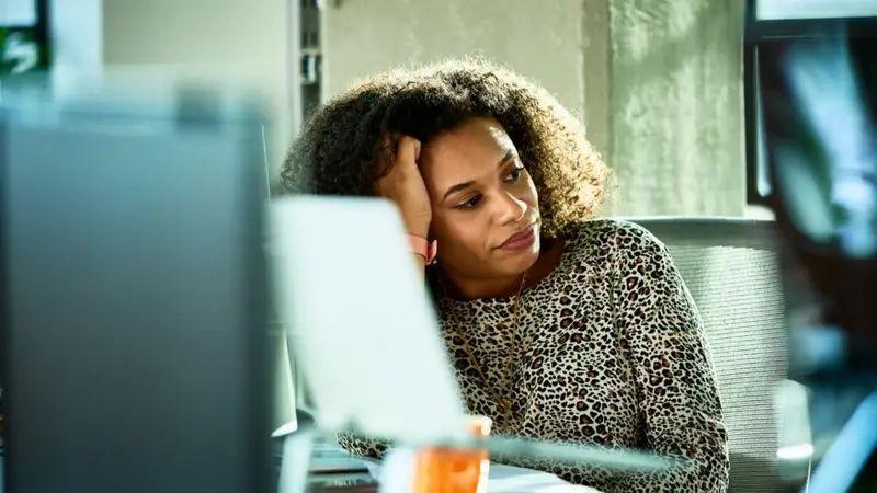 Uma mulher negra em frente a um computador olhando para o lado