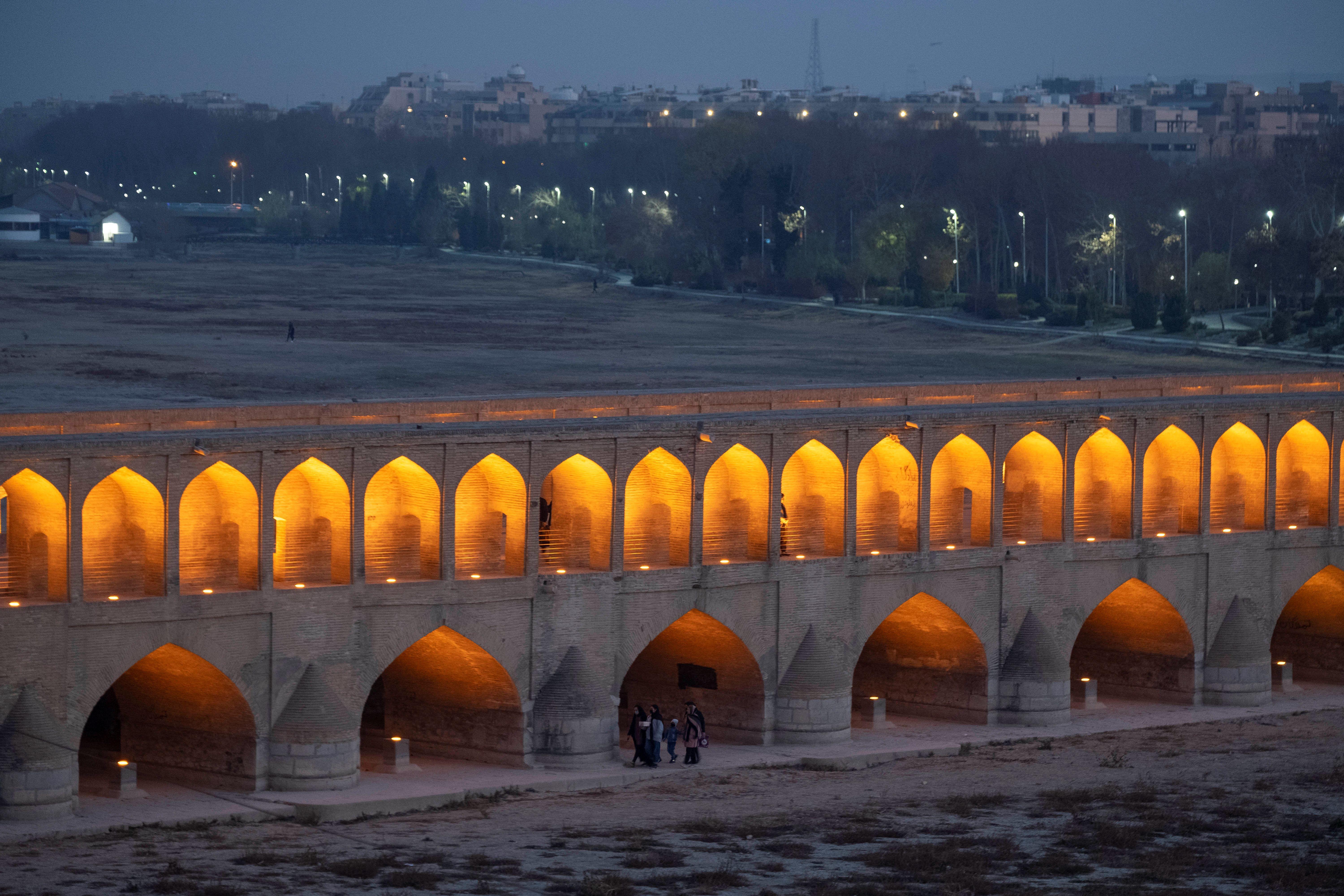 Iluminado al anochecer, el Puente de los 33 Arcos de principios del siglo XVII de la ciudad de Isfahán se extiende sobre el lecho seco del río Zayandeh Rud, mientras un grupo de peatones lo cruza.