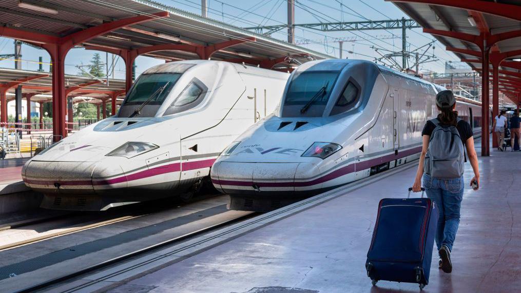 Una mujer, de espaldas, arrastra su maleta hacia un tren de alta velocidad estacionado en la estación de Chamartín, Madrid.