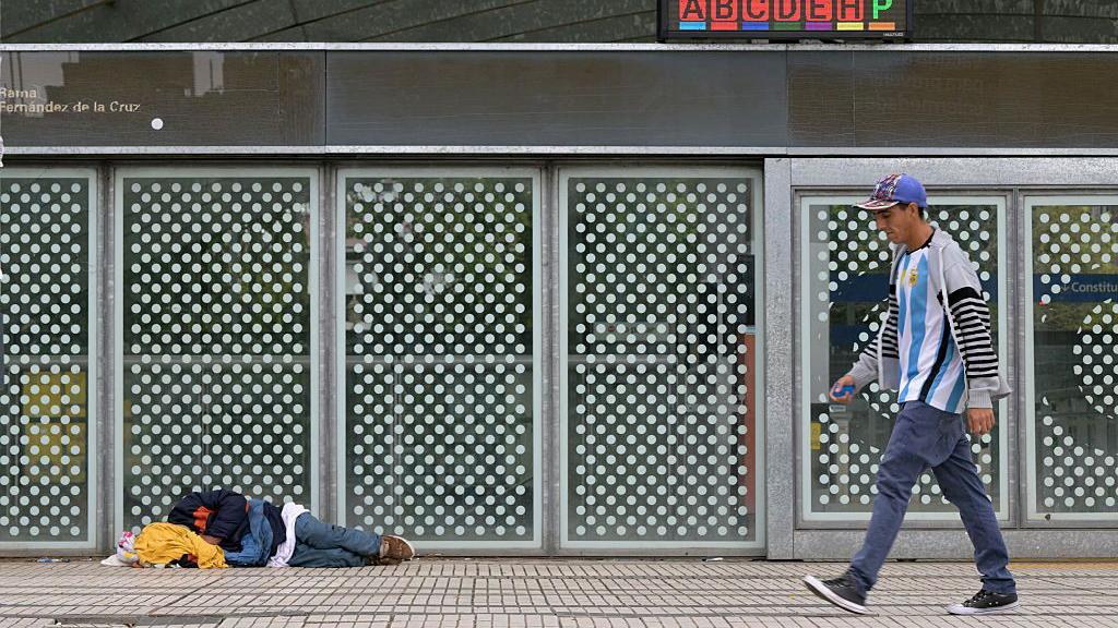 Un hombre pasa frente a la estación de metro Constitución, en Buenos Aires, mientras una persona duerme en el suelo.