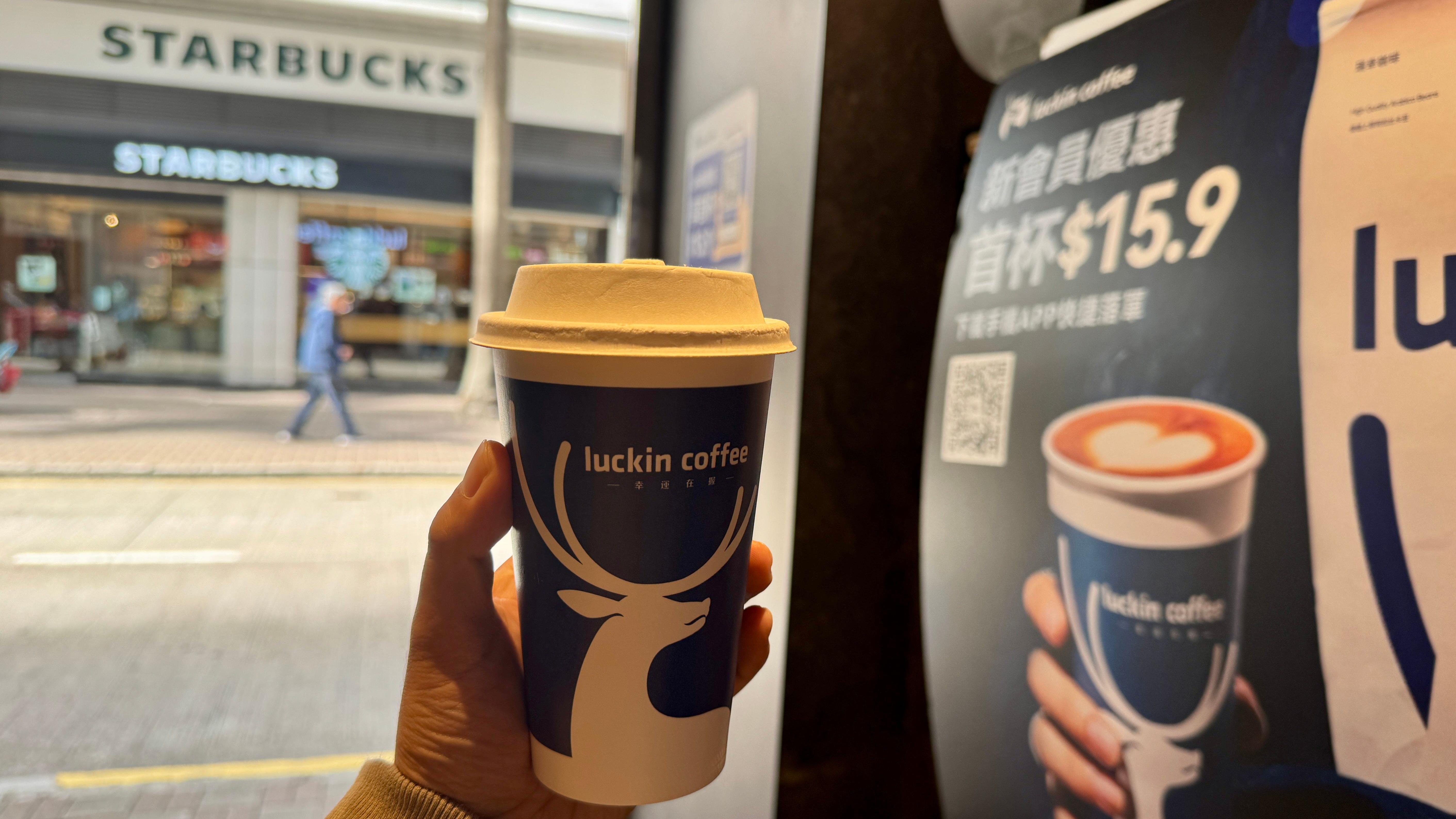 手中舉著一杯瑞幸咖啡。