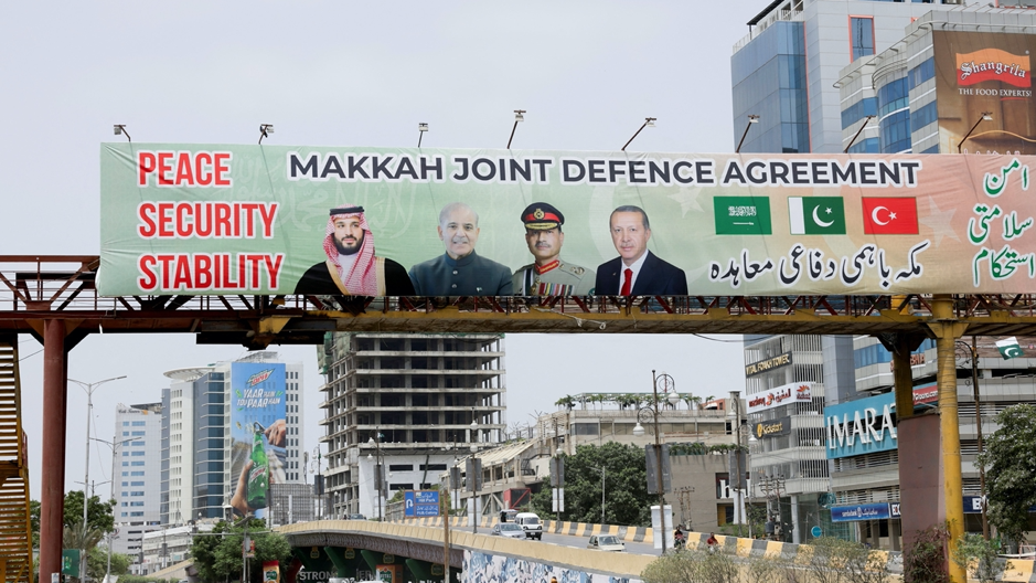 Una valla publicitaria sobre el tráfico muestra a los líderes de Turquía, Arabia Saudita y Pakistán tras la firma del Acuerdo Conjunto de Defensa de La Meca, en Karachi. Debajo se ven coches y personas. 