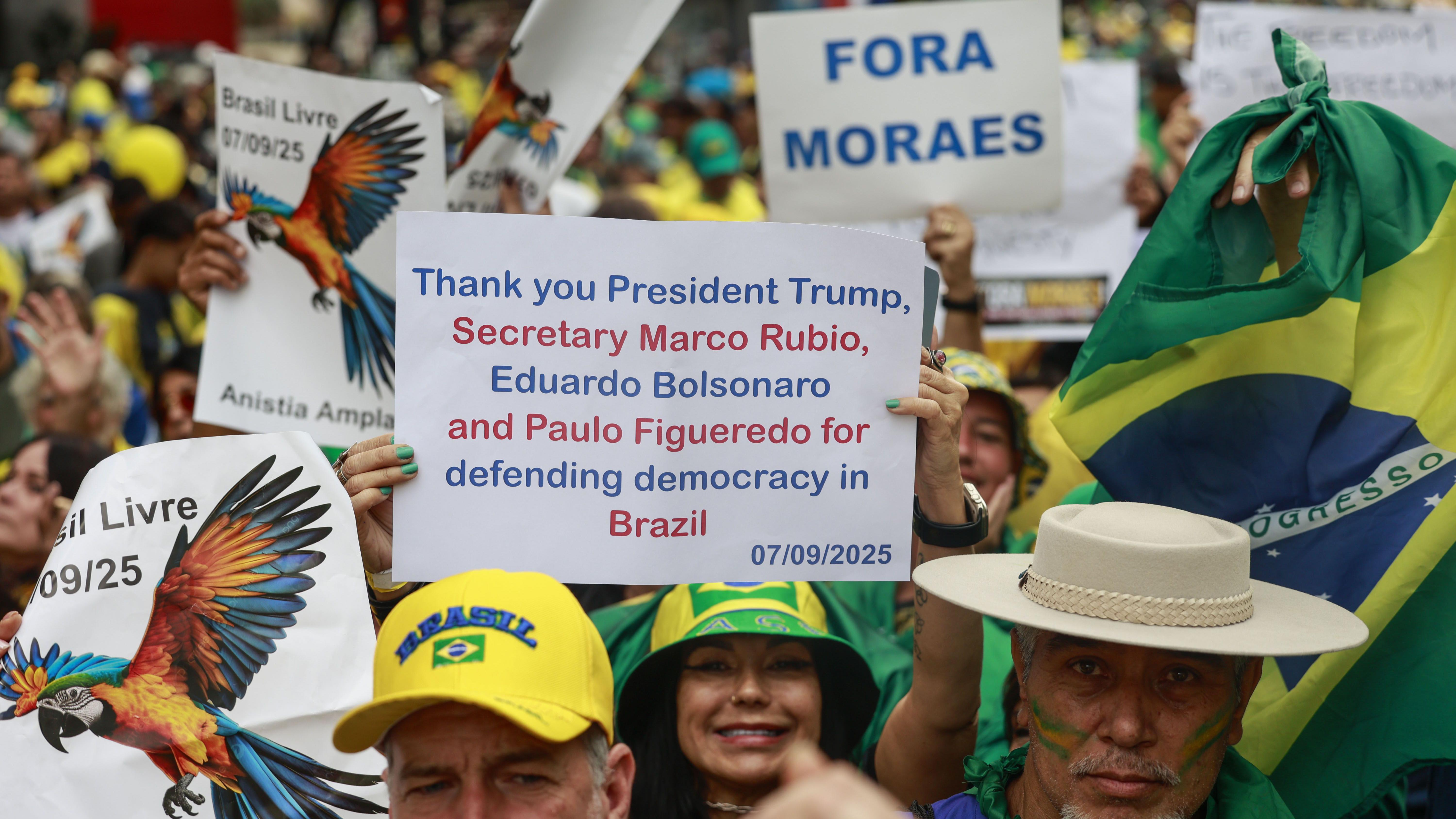 Mulher segura cartaz agradecendo Trump, Marco Rubio, Eduardo Bolsonaro e Paulo Figueredo por 