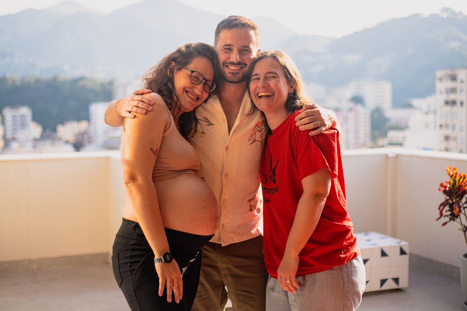 Carol, Eduardo e Renata abraçados e sorrindo em cobertura de prédio