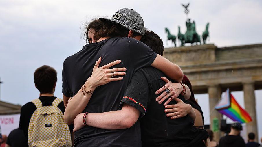 Un grupo de jóvenes se abraza ante la puerta de Branderburgo.