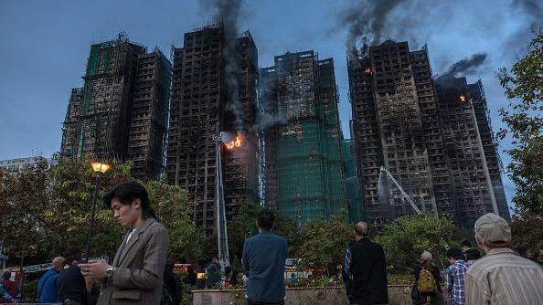 2025年11月26日，香港大埔區宏福苑住宅大樓發生大火，濃煙從公寓大樓內升起。屋苑外有多名巿民站著，或看著火勢，或盯著電話屏幕。