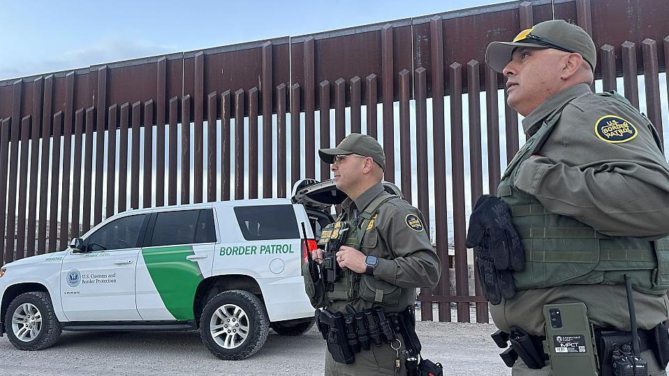 Dos oficiales de la Patrulla Fronteriza junto al muro que divide EE.UU. de México.