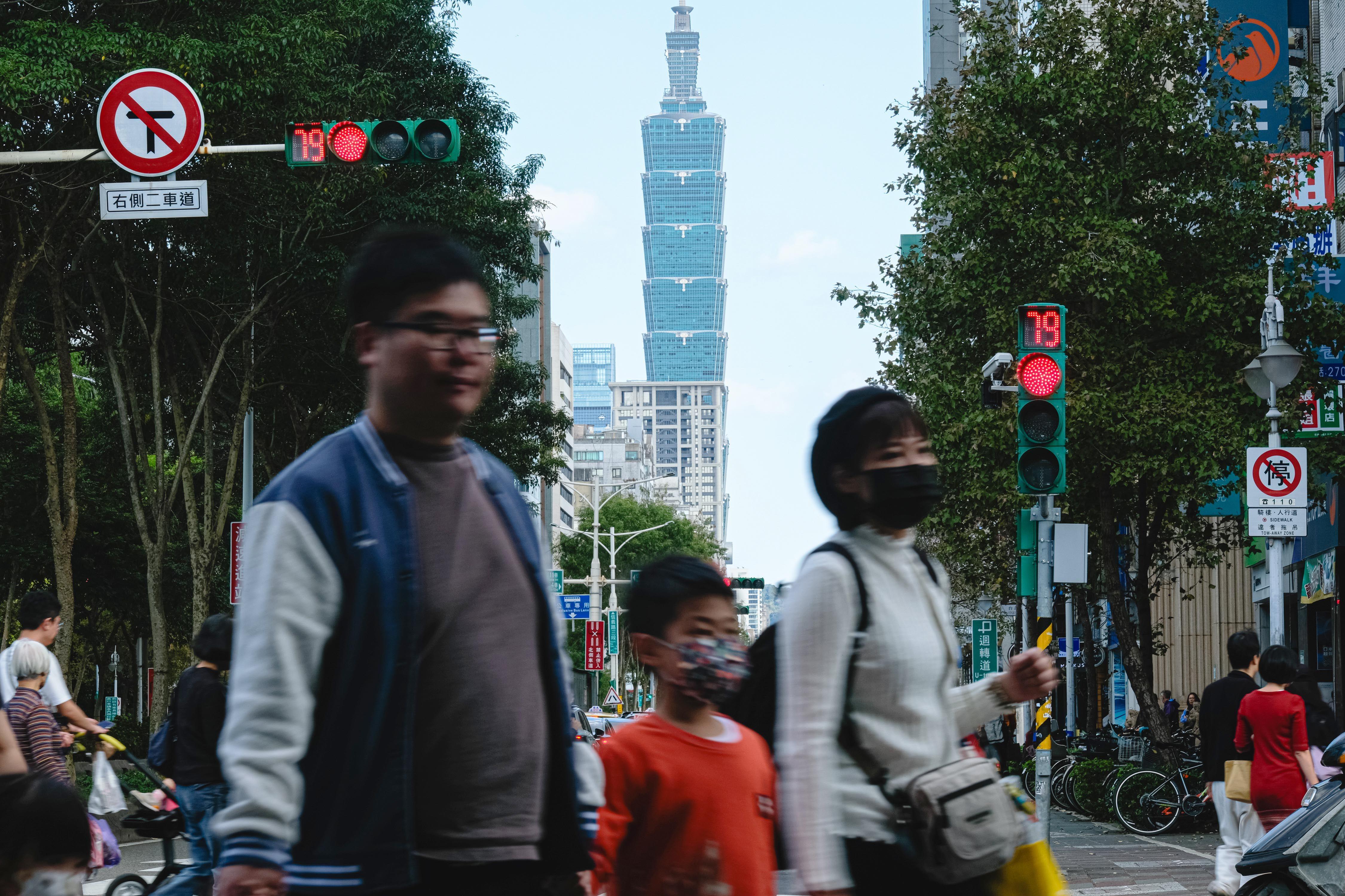 台北的街頭景象，前方是一些路人橫過馬路，背景是台北101大樓。
