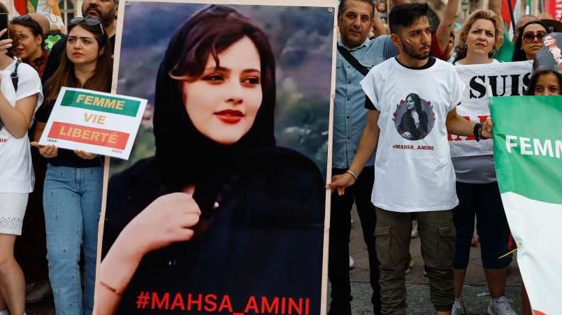 أشخاص يتظاهرون حاملين لافتات وصورة لـ مهسا أميني