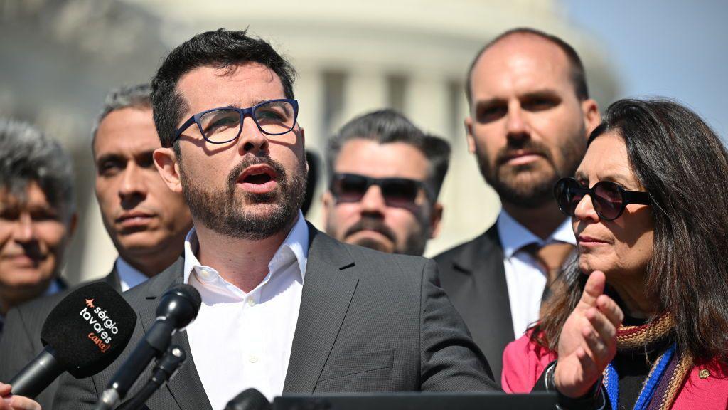 Paulo Figueiredo discursa, com Eduardo Bolsonaro no fundo. 