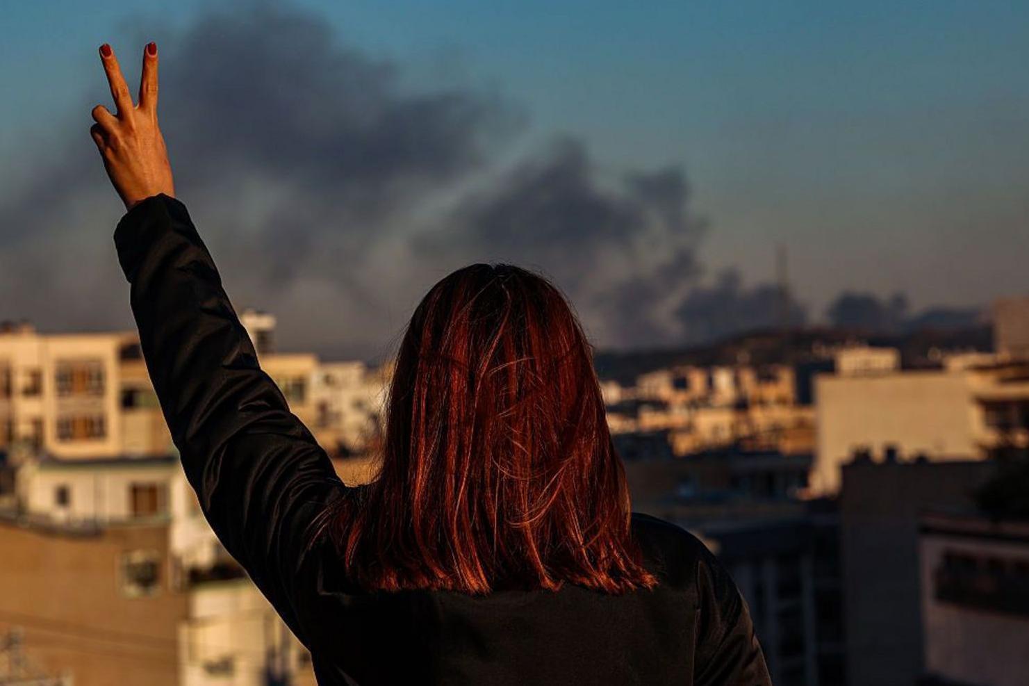امرأة تراقب عموداً من الدخان وترفع علامة النصر