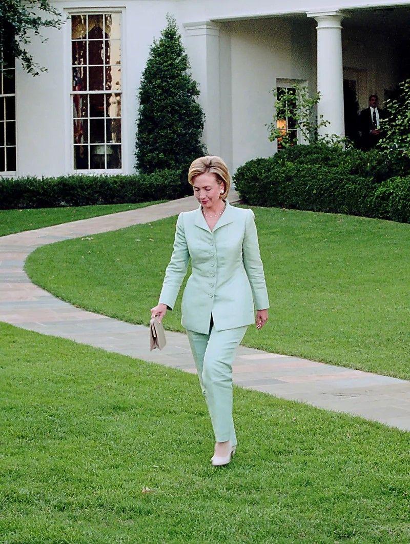 Hillary Clinton caminhando em um jardim. Ela usa um conjunto verde claro 
