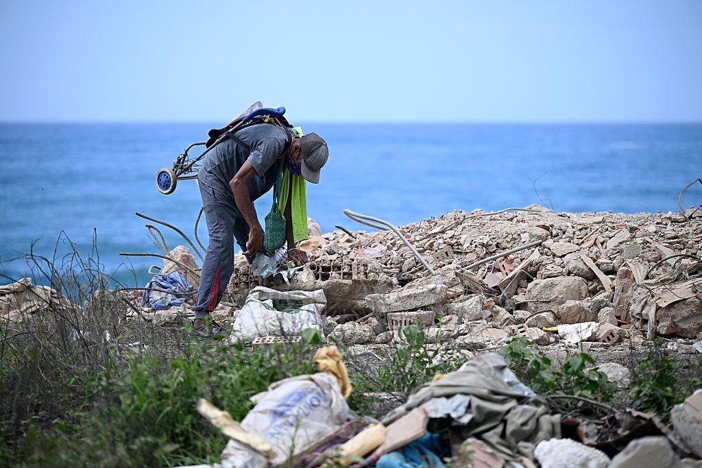 Un hombre se agacha y parece buscar entre los escombros que dejó el sismo. Detrás, el mar. 