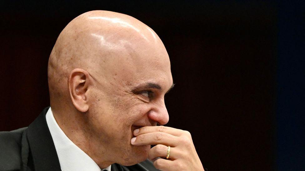 Aleksandar de Moraes u sudijskoj crnoj odori i beloj košulji drži ruku preko usta  
