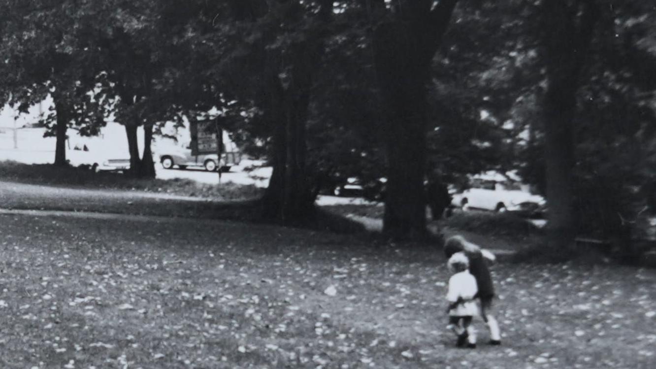 Uma foto em preto e branco de duas crian&ccedil;as pequenas de m&atilde;os dadas caminhando em um parque