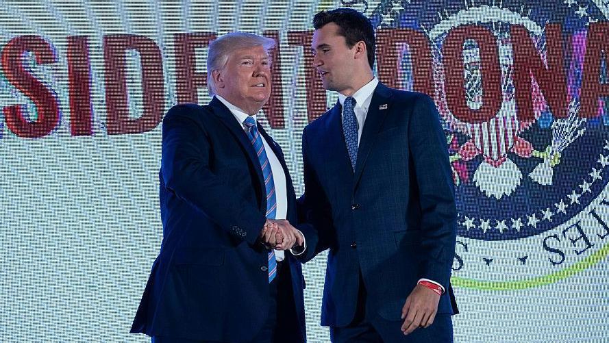 Donald Trump y Charlie Kirk se dan la mano en un escenario.
