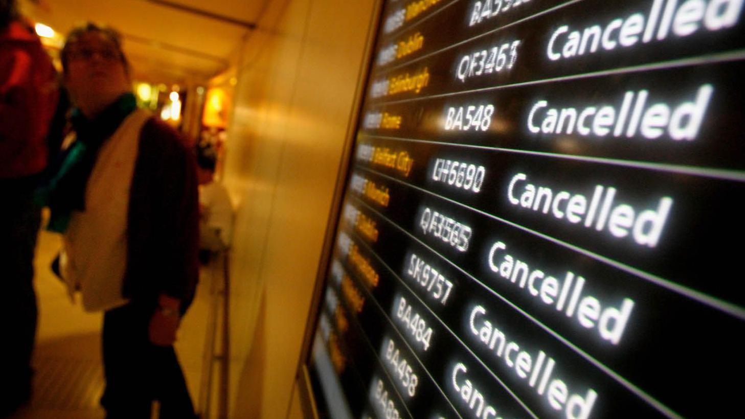 Vista de um terminal de aeroporto com um grande painel eletr&ocirc;nico de partidas com v&aacute;rias listas de voos, todos marcados como &ldquo;Cancelled&rdquo; (cancelado) em letras brancas sobre fundo escuro, com n&uacute;meros de voos vis&iacute;veis