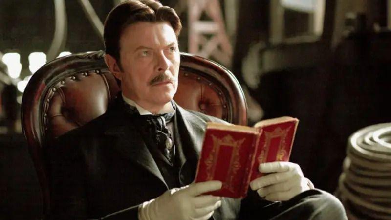 Dejvid Bouvi sa brkovima u odelu drži crvenu knjigu