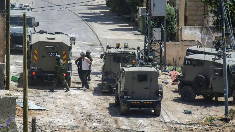 صورة تُظهر جنودا إسرائيليين يقفون قرب سيارات عسكرية ويقومون بتكبيل فلسطيني في الضفة الغربية