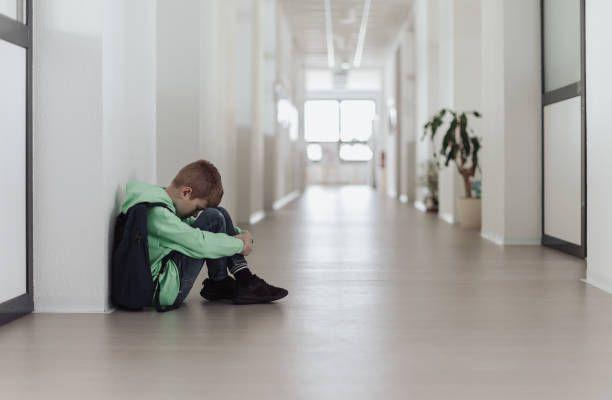 طفل يجلس على الأرض داخل أحد الممرات ويضع رأسه بين رجليه