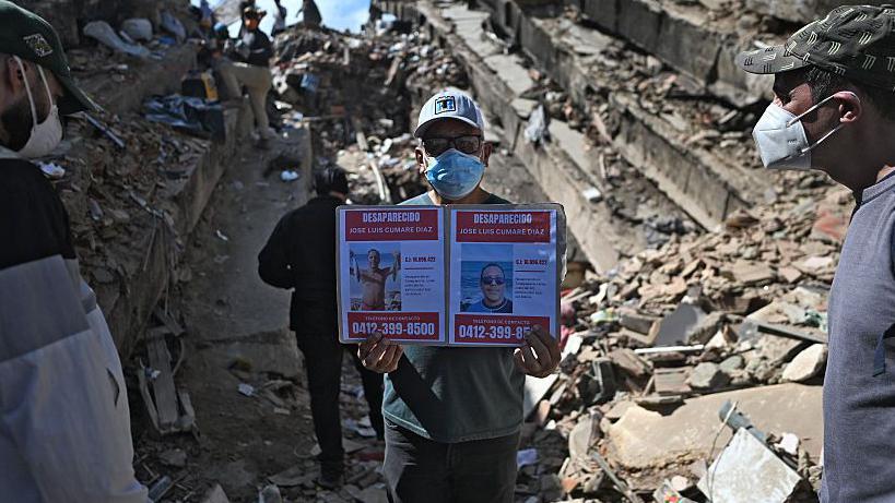 Hombre entre escombros mostrando las fotos de dos desaparecidos. 
