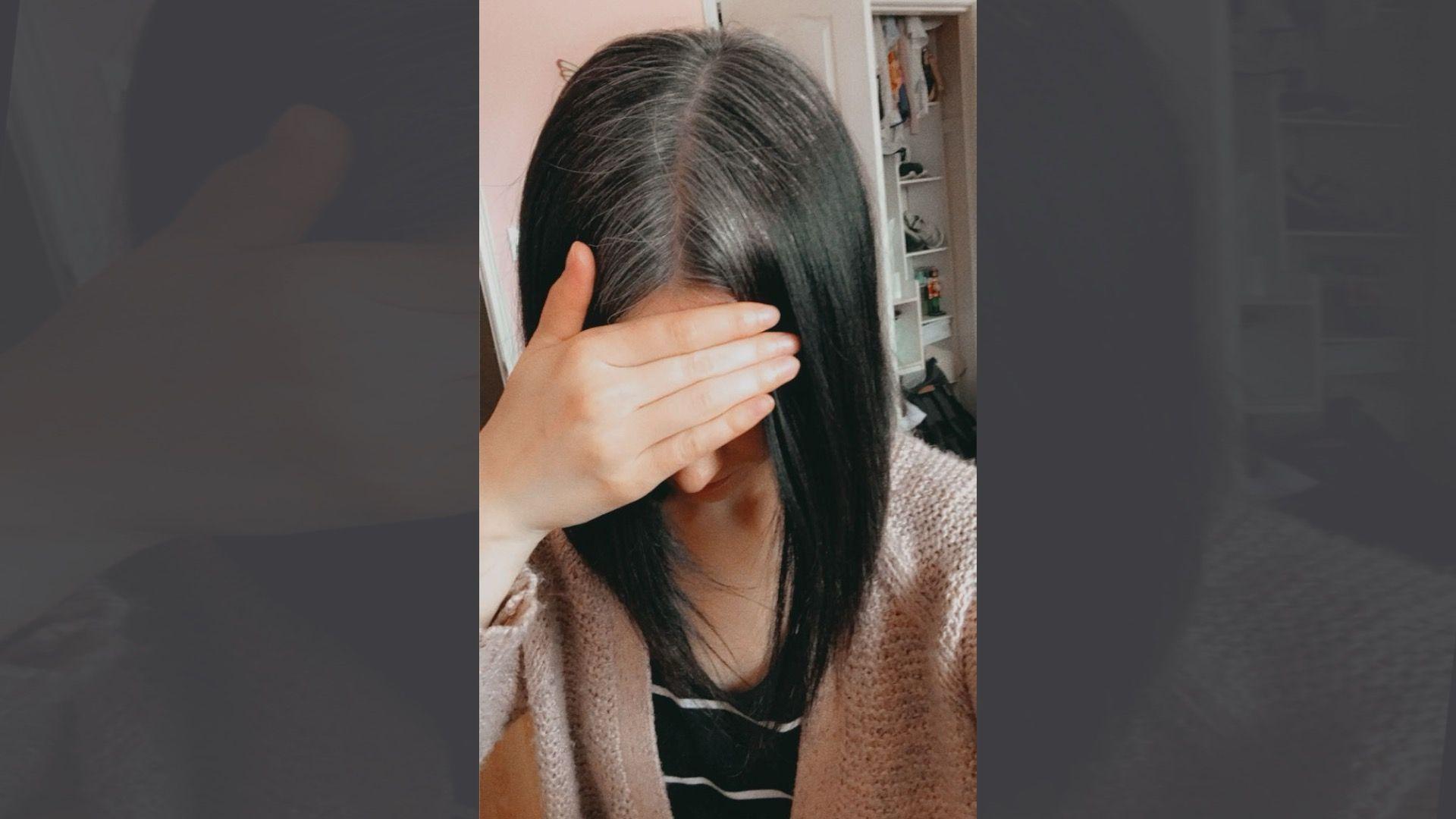 阿什莉·蘇克魯的自拍照。她有一頭及肩的深色直髮，髮縫處開始轉為灰白色。她低著頭，用手遮住眼睛。她穿著黑白條紋T恤和一件米色針織外套。