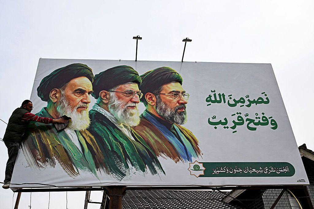 Um homem limpa um cartaz com as imagens dos falecidos l&iacute;deres supremos do Ir&atilde;, o aiatol&aacute; Ruhollah Khomeini (&agrave; esquerda) e o aiatol&aacute; Ali Khamenei (ao centro), ao lado do rec&eacute;m-eleito l&iacute;der supremo, o aiatol&aacute; Mojtaba Khamenei