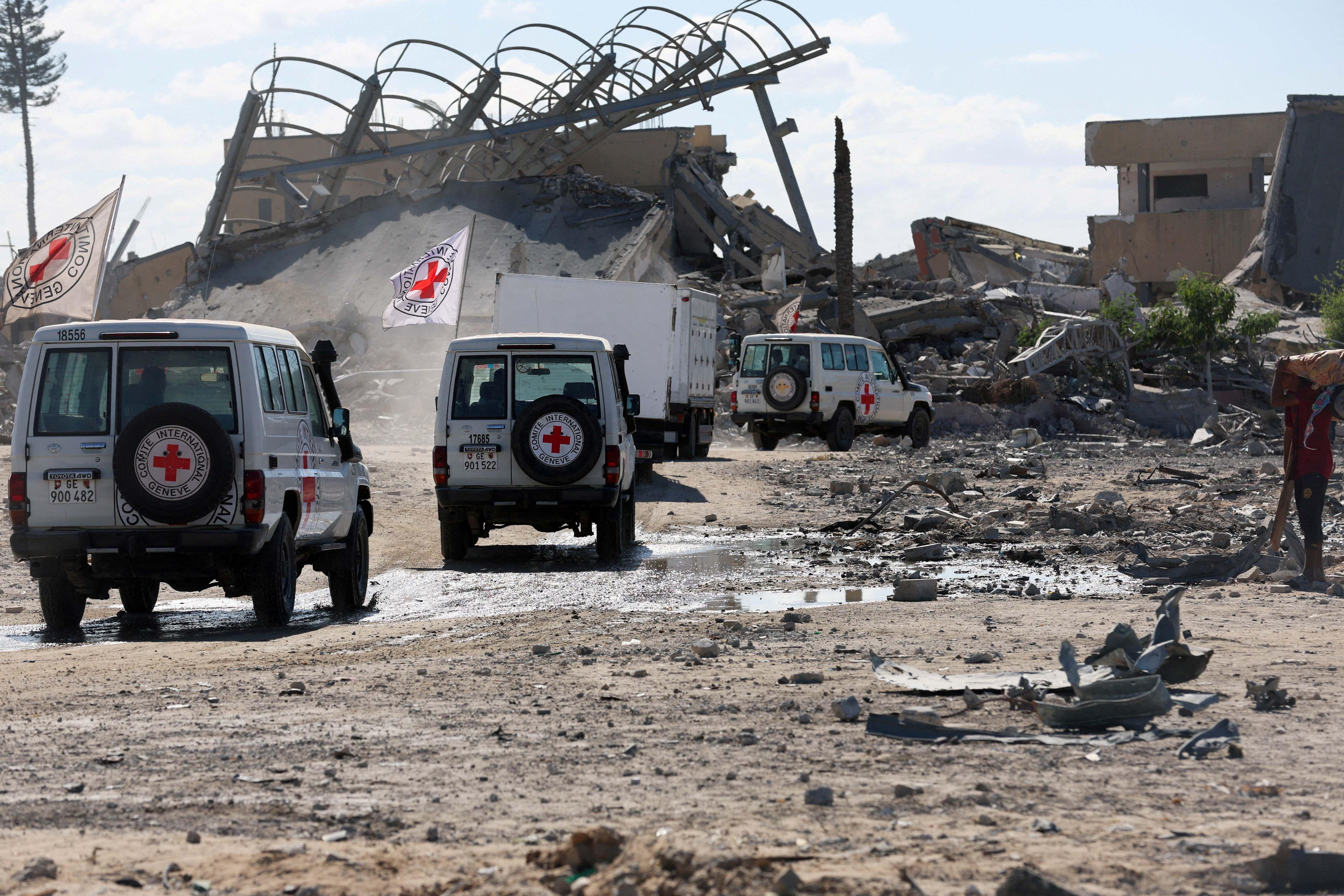 Varios vehículos de la Cruz Roja Internacional escoltan a un camión frigorífico que transporta cadáveres de palestinos. Están en Gaza y pasan por delante de las ruinas de unos edificios.
