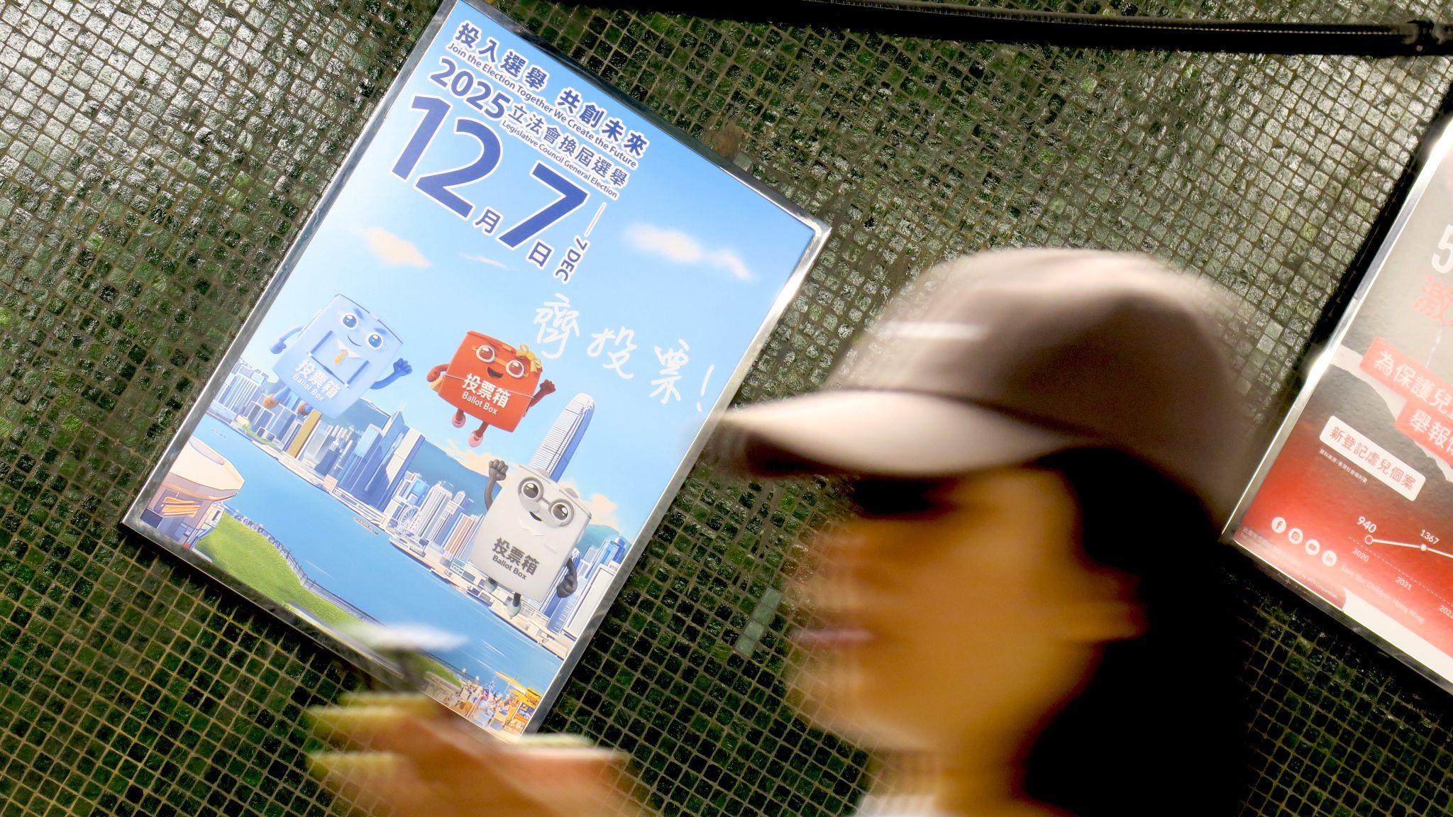 港鐵炮台山站內一位女士在扶手電梯上查看手機，背景是宣傳12月7日香港立法會選舉投票的官方海報（BBC中文圖片4/12/2025）