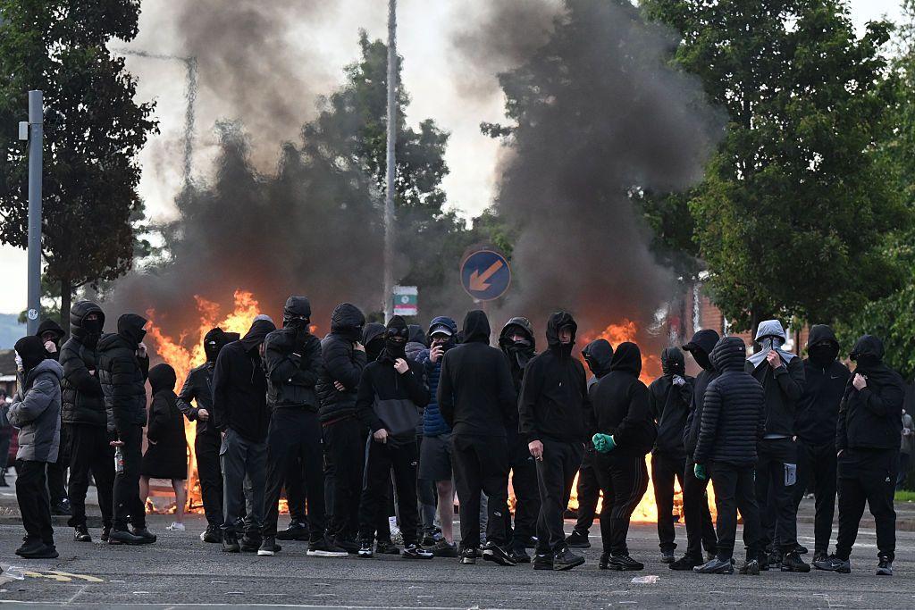 Jóvenes encapuchados con fuego detrás.