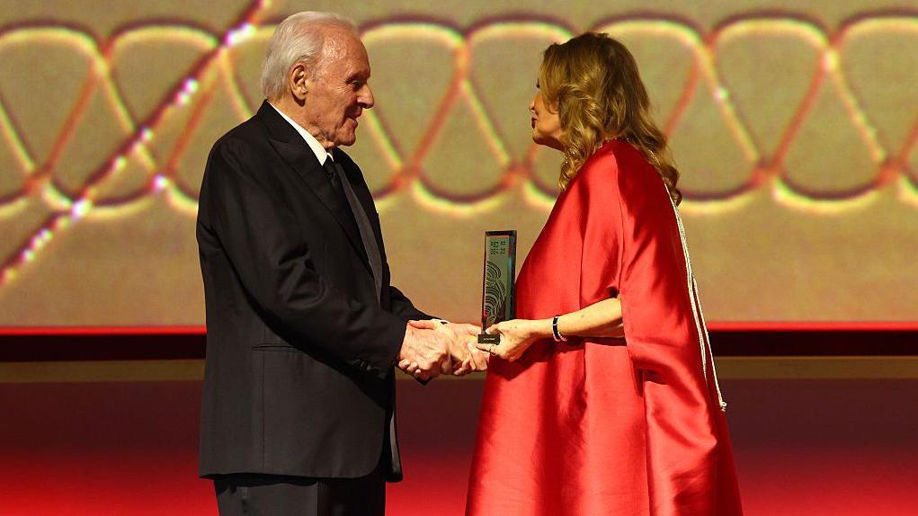 يسرا الممثلة المصرية (يمين) بثوب أحمر تقدم جائزة لأنتوني هوبكينز - بزة رسمية سوداء