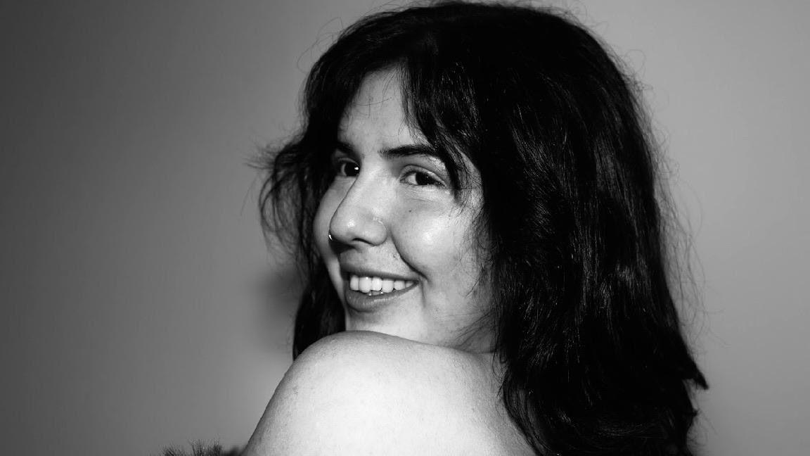 A black and white close-up photo of a young woman smiling over her shoulder.