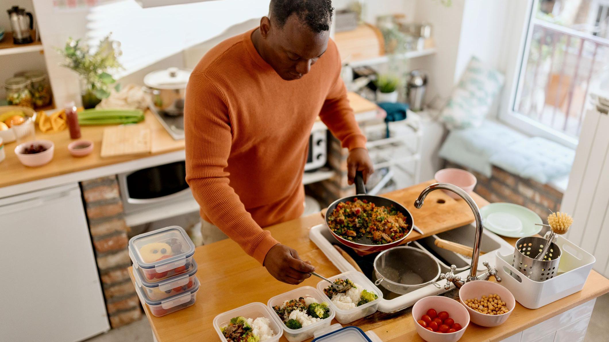 Homem preparando marmitas com bastante salada e grãos
