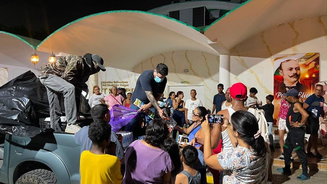 Víctor y su equipo entregando comida en La Guaira. Están montados en una camioneta rodeados de gente tomando fotos y recibiendo comidas. 