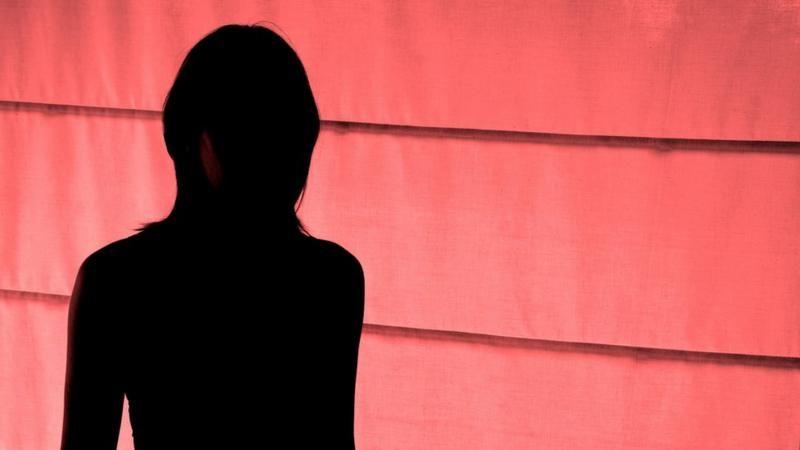 Vulto de mulher em pé, em frente a uma parede vermelha