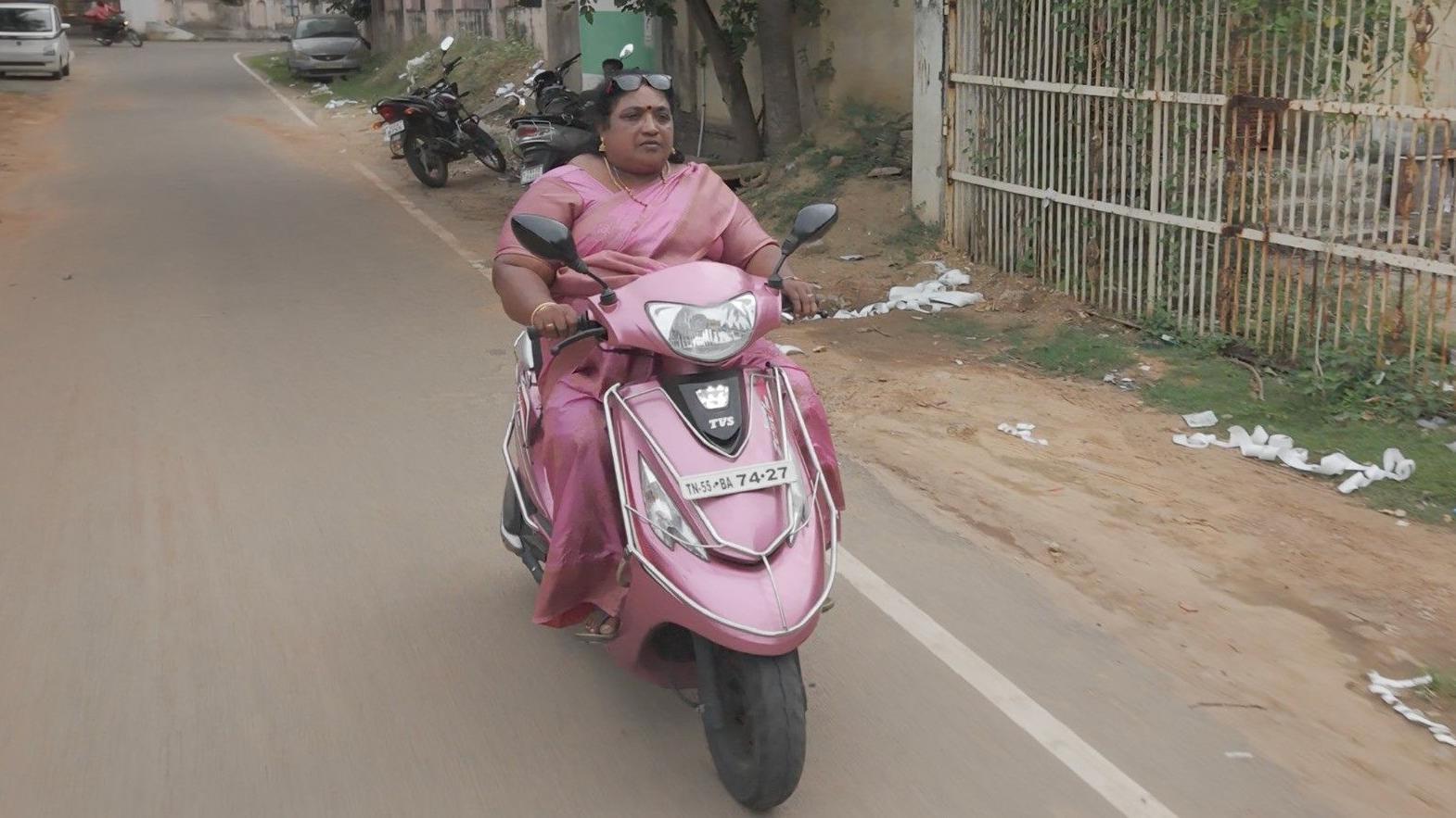 Jayachithra com um s&aacute;ri rosa, andando em uma lambreta rosa pela sua vizinhan&ccedil;a