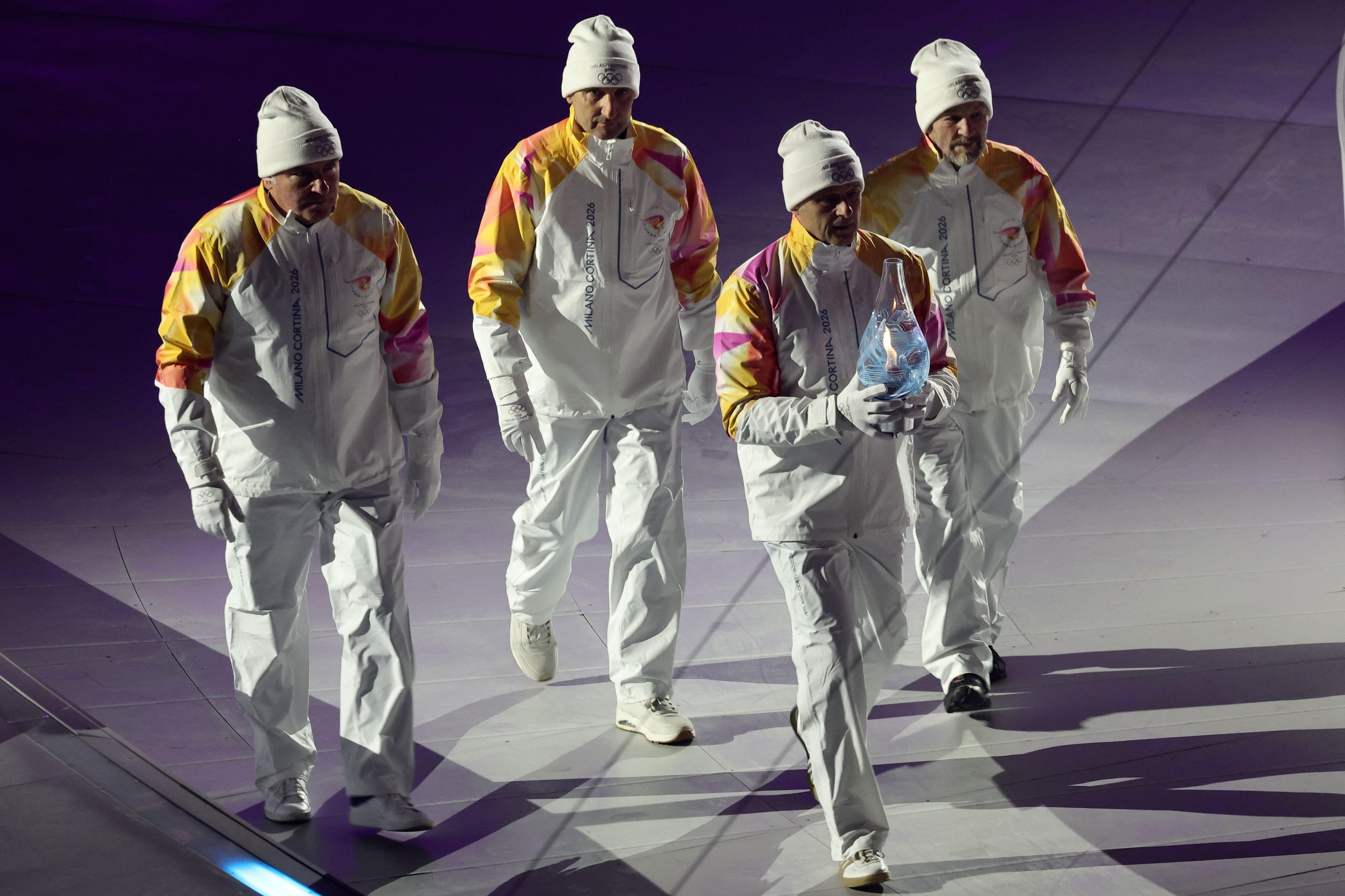 Četvorica muškaraca u belim odelima i sa belim kapama na glavama, olimpijski šampioni iz Lilehamera 1994. godine, u štafeti 4x10 km u skijaškom trčanju, nose olimpijski plamen