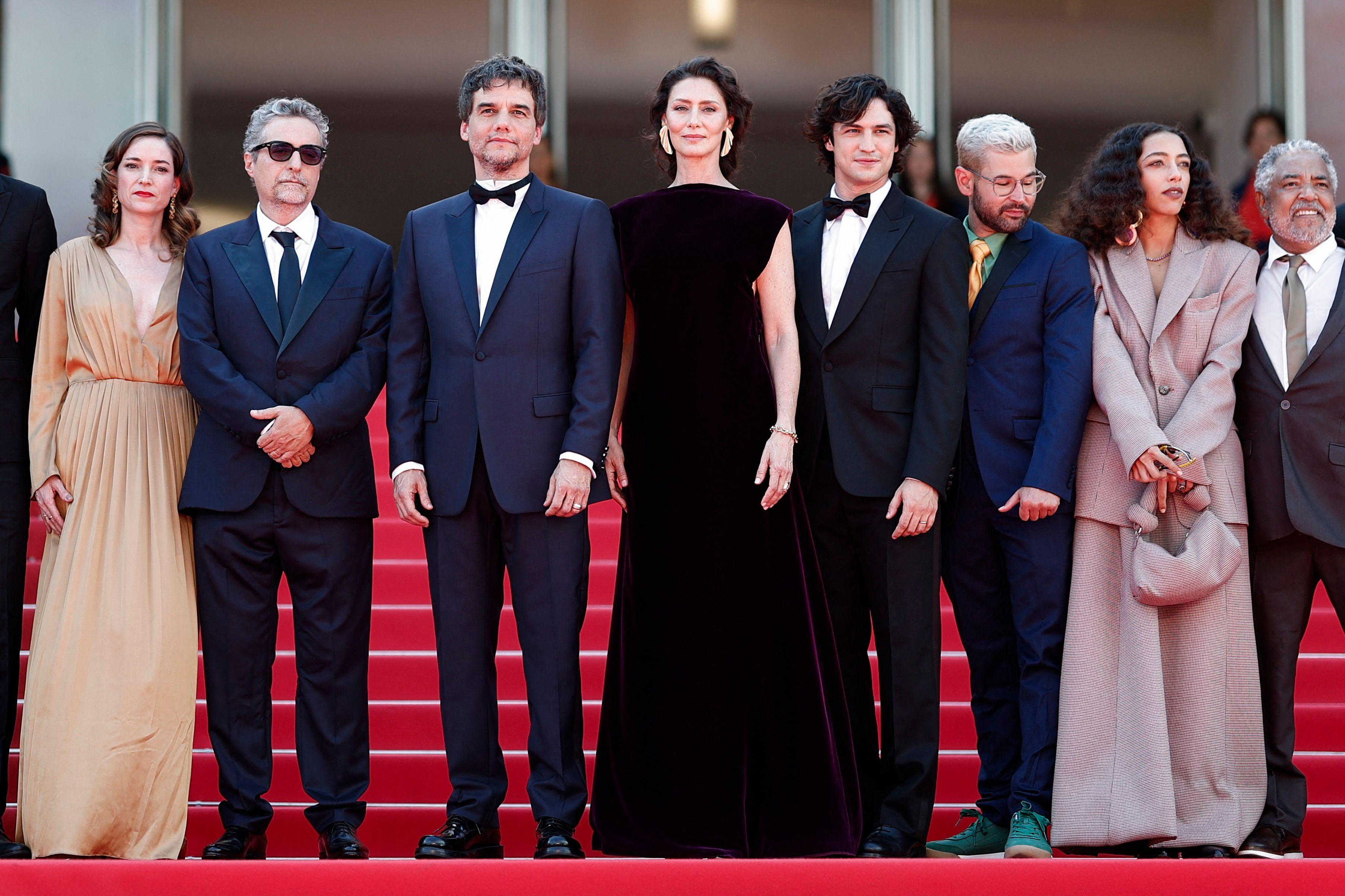 Oito pessoas em pé em frente à uma escada vermelha. Entre elas está Wagner Moura, de terno e gravata.