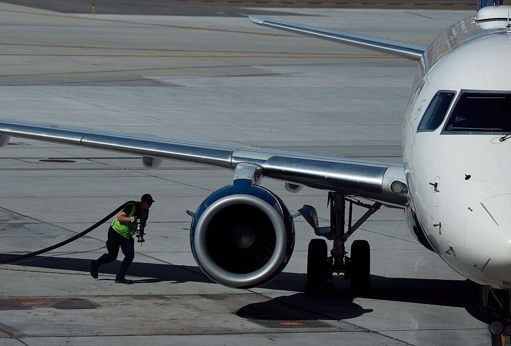 Un técnico carga una manguera bajo el ala de un avión, momentos antes de conectarla para llenarlo con combustible.