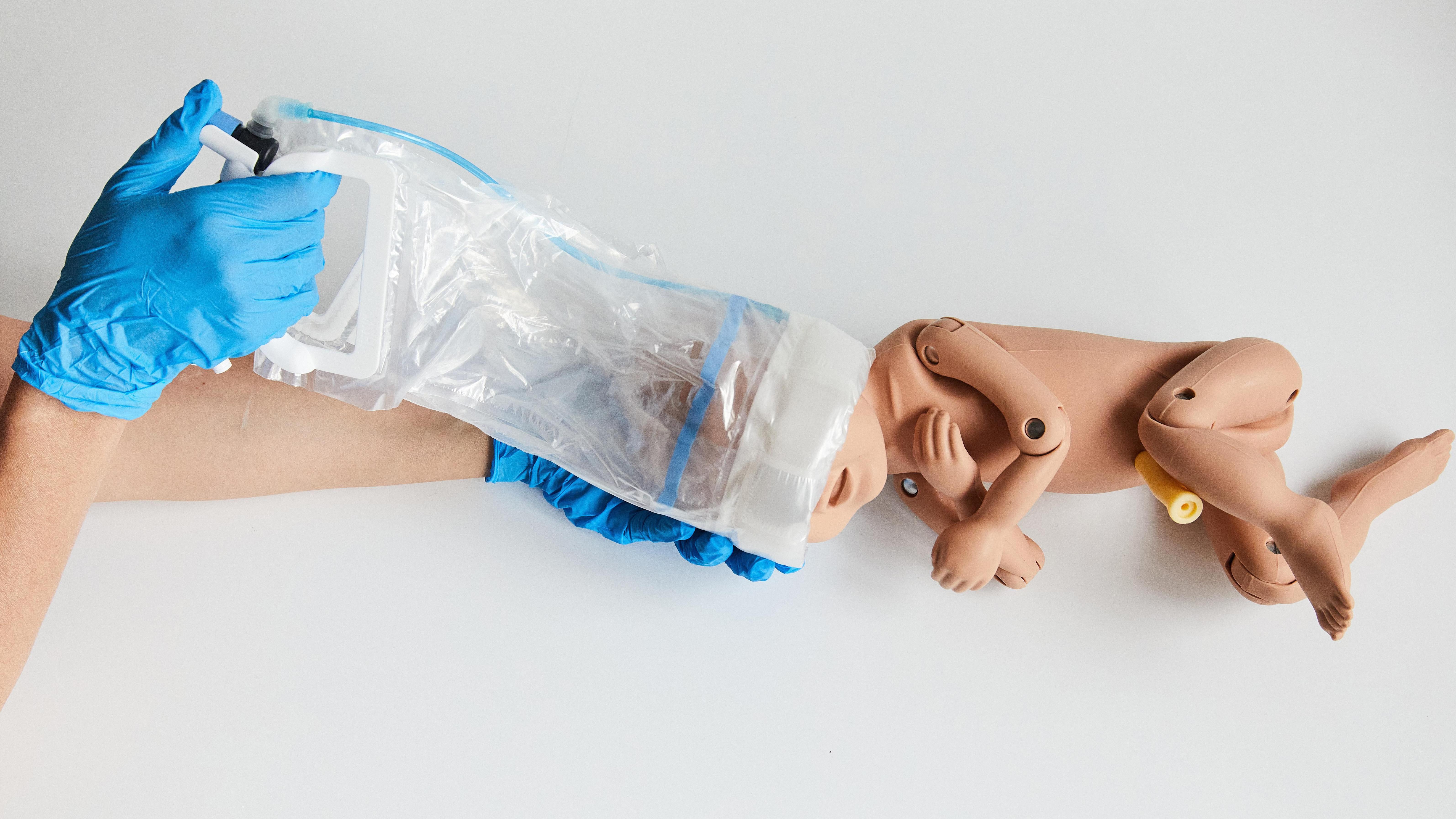 Una persona que lleva guantes azules está utilizando el dispositivo OdonAssist y dentro de él un muñeco de un bebé.