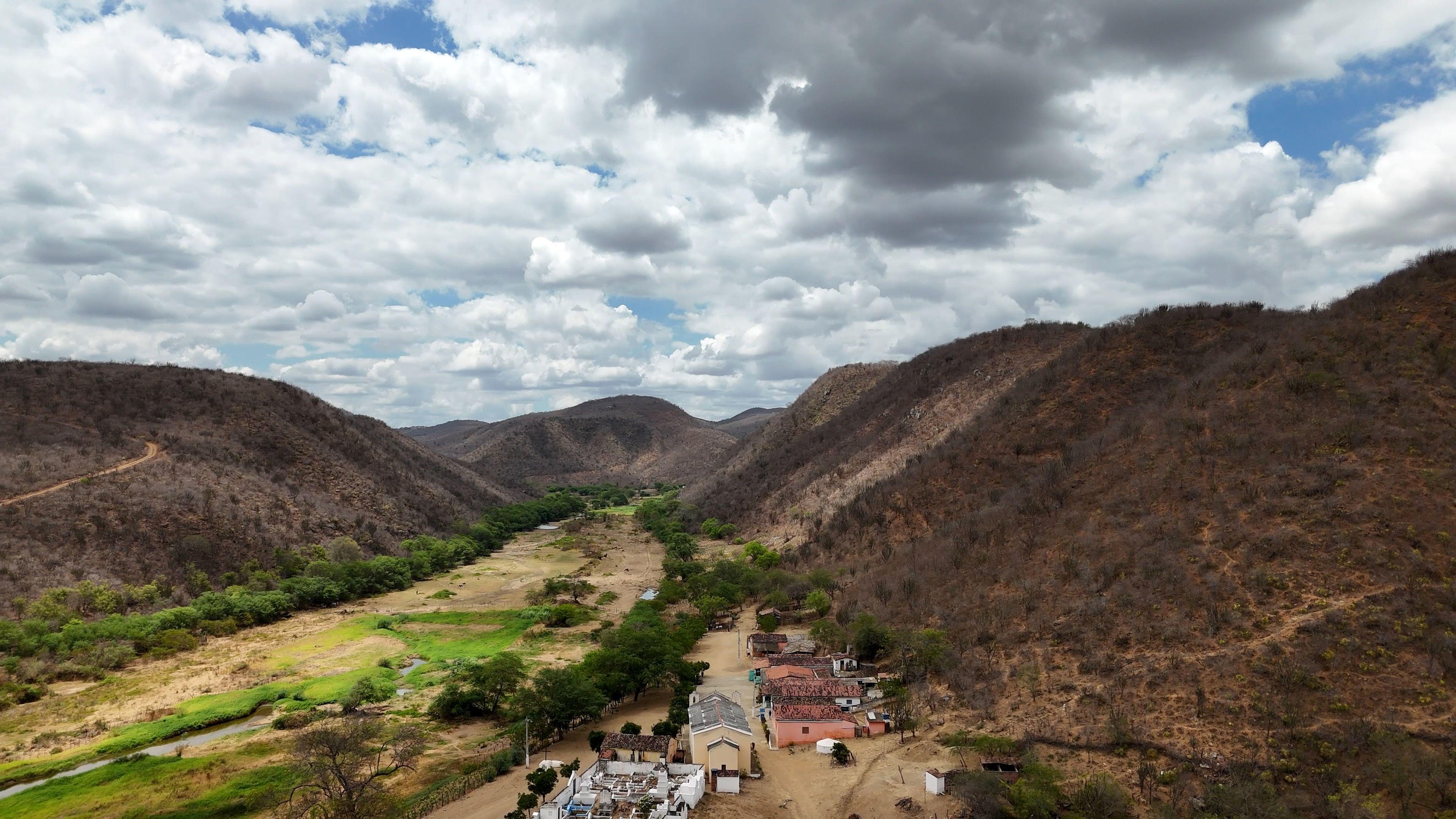 Povoado localizado em vale com margens esverdeadas; em volta, há morros com paisagem semiárida