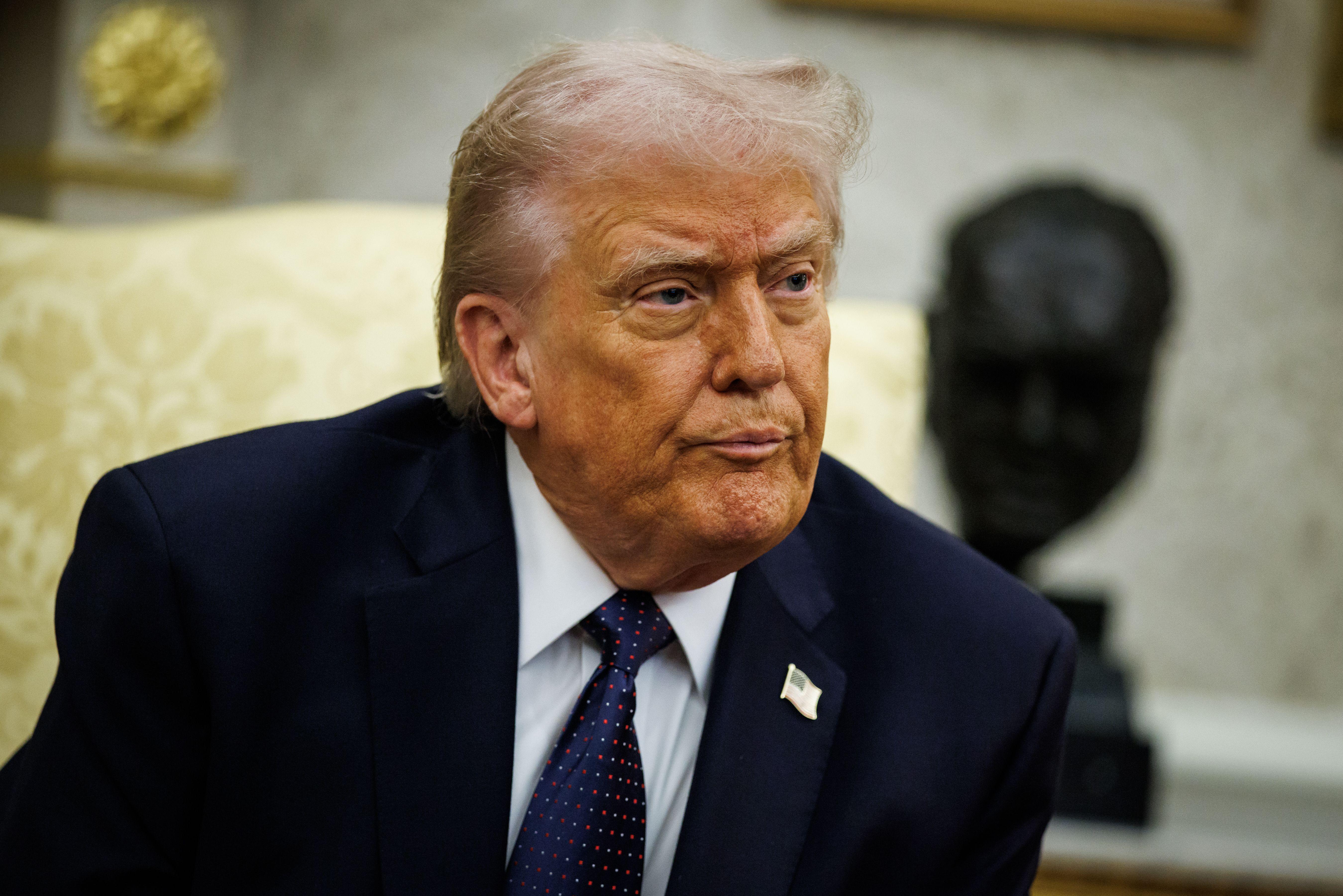 الرئيس ترامب يرتدي بدلة رسمية كحلية ودبوساً صغيراً عليه العلم الأمريكي وقميصاً أبيض اللون وربطة عنق كحلية منقطة باللونين الأحمر والأبيض.