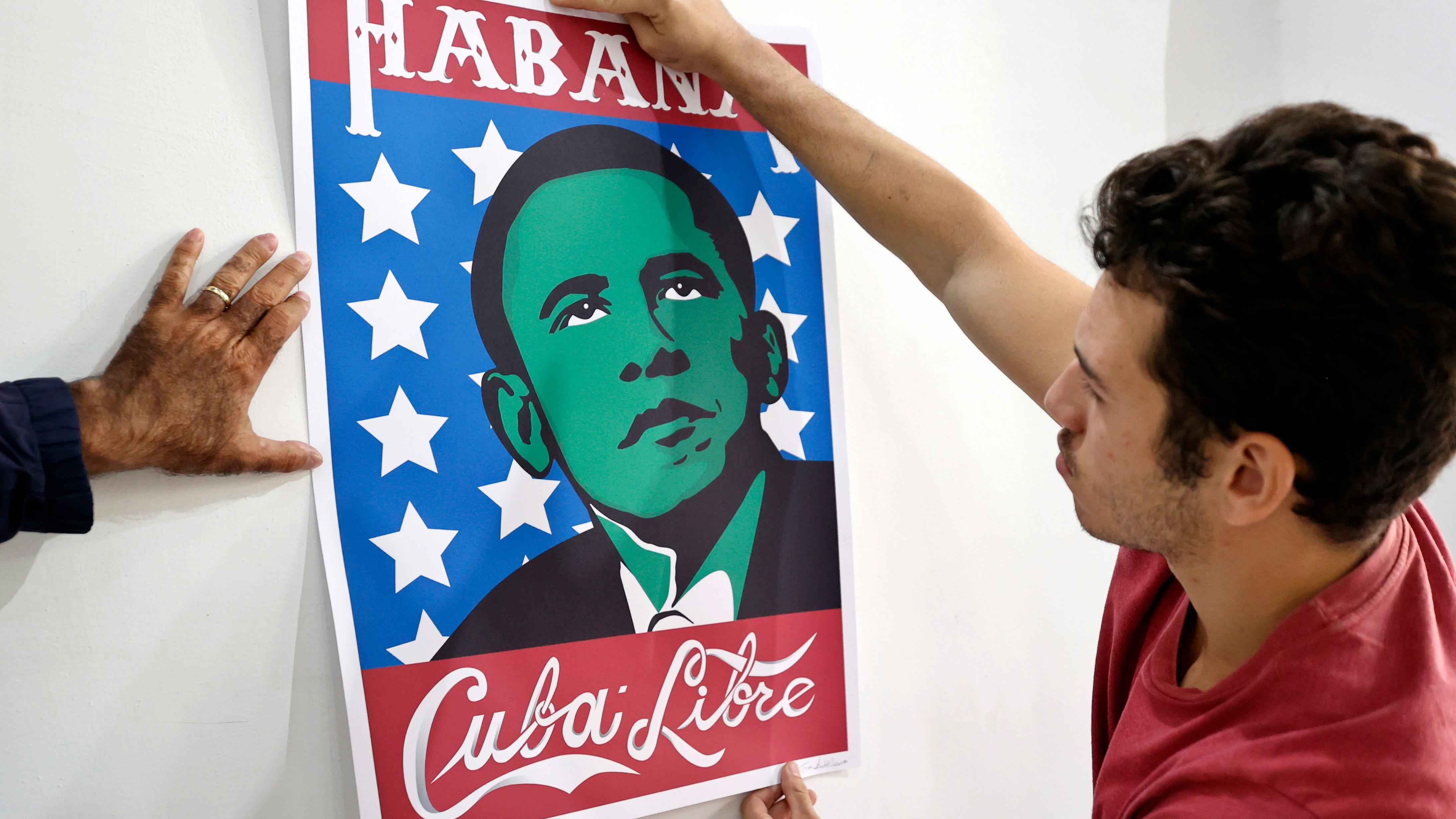 Fotografija prikazuje muškarca koji postavlja plakat s karikaturom Baraka Obame i natpisom „Habana - Cuba Libre“, povodom obeležavanja desete godišnjice istorijskog pokušaja pomirenja dve zemlje 2014. godine.