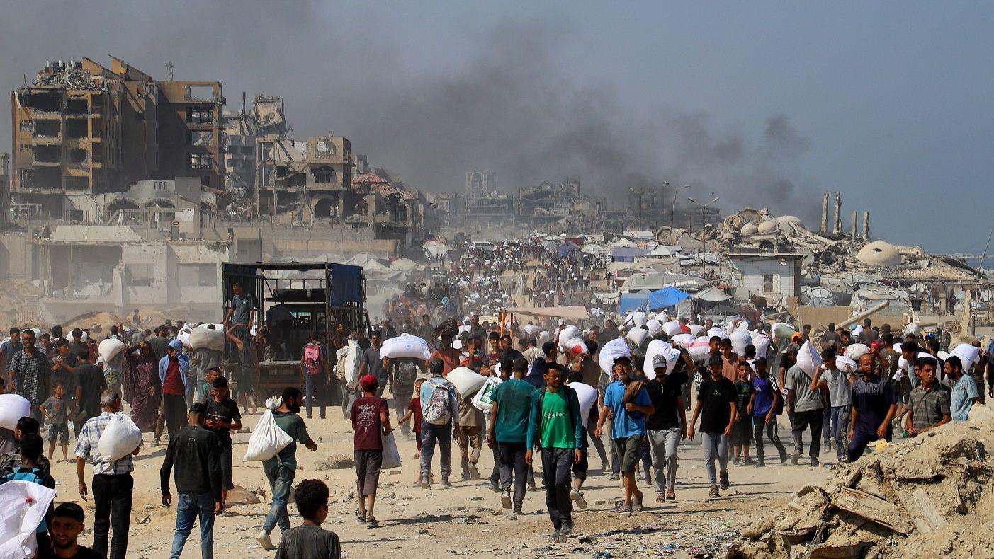 هل تنقذ "الهدنة الإنسانية" الفلسطينيين في غزة من "المجاعة"؟ 2 أشخاص يحملون مساعدات في غزة.